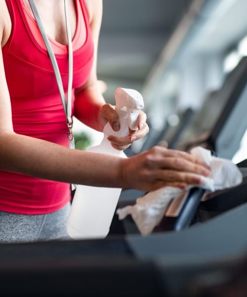 A midsection of fitness woman instructor disinfecting equipment in gym, coronavirus concept.